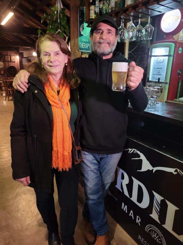 Na foto, aparece um casal, o home está segurando uma taça de chopp.