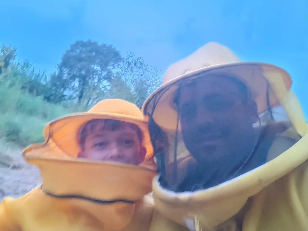 Na foto, há duas pessoas com roupas específicas da apicultura